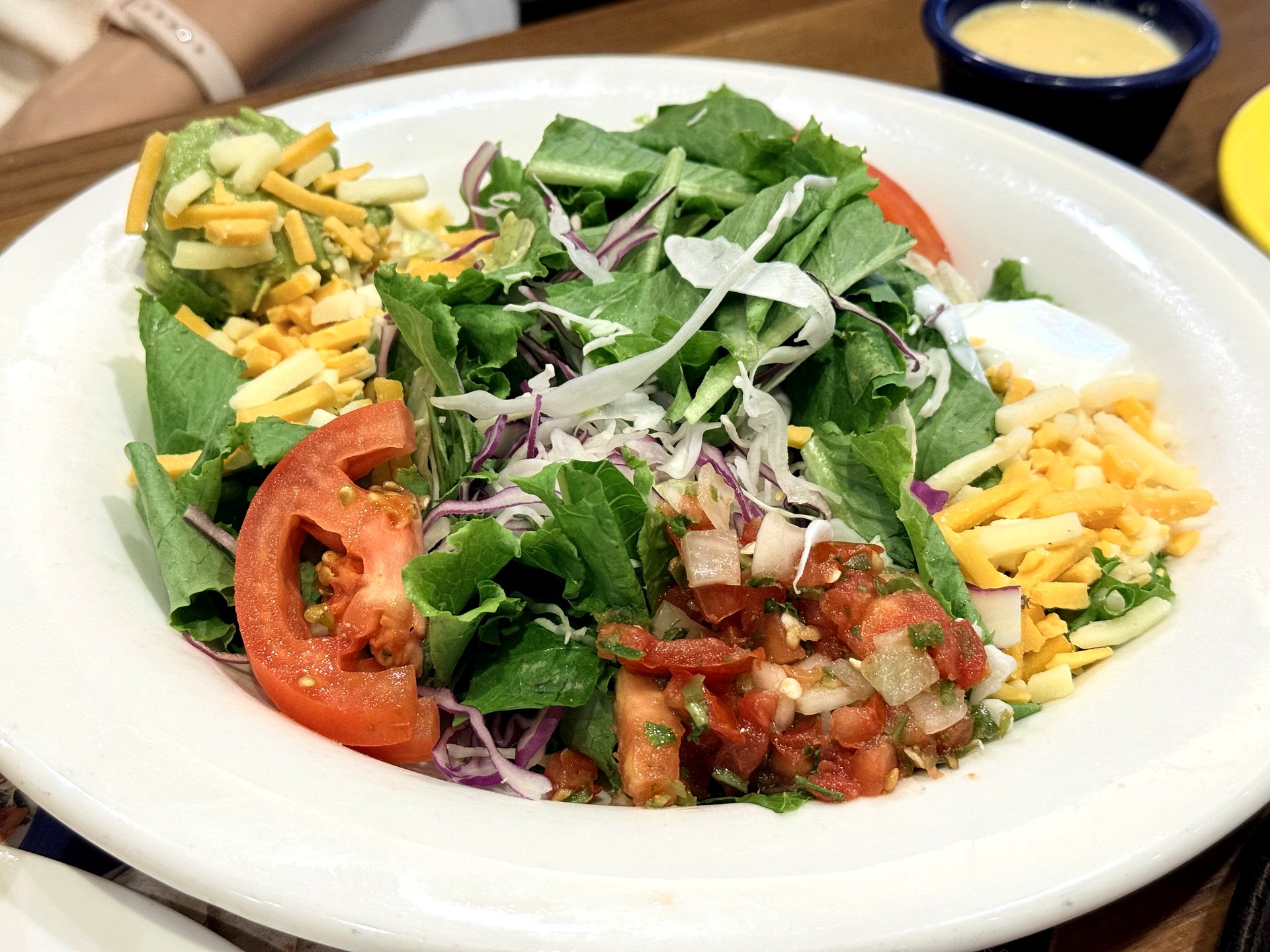 On The Border taco salad - a large bowl of crisp lettuce and cabbage topped with tomato wedges, shredded cheddar and jack cheese, guacamole and pico de gallo, with a cup of honey-mustard dressing