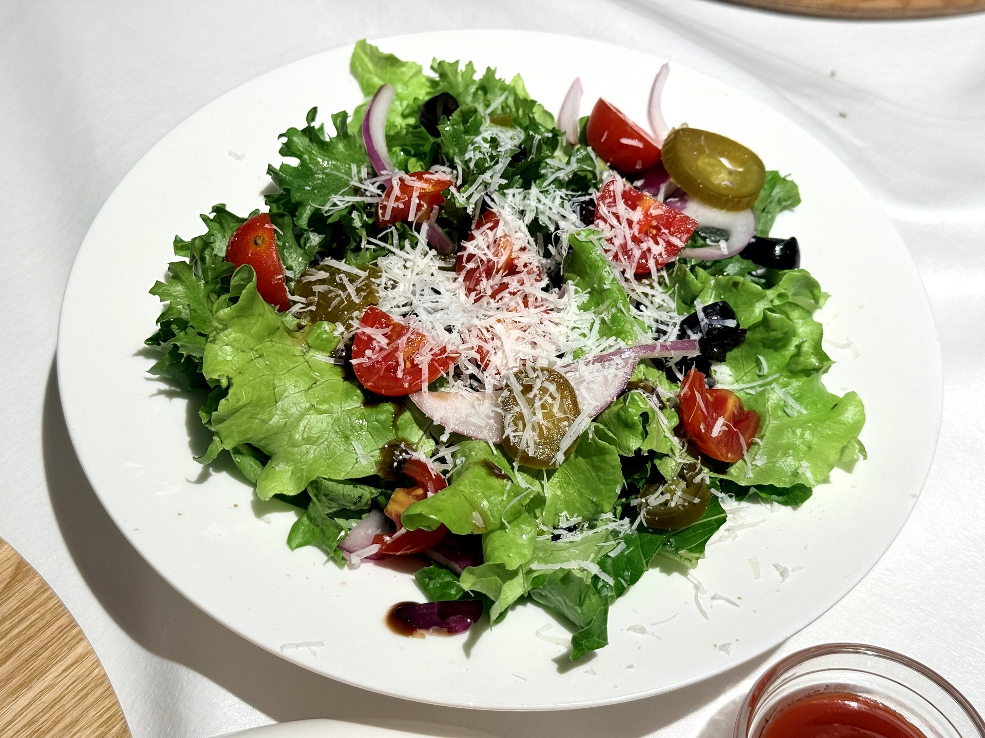 OZ Pizza house salad - crisp lettuce, cherry tomatoes, olives, red onion and grated parmesan with balsamic dressing on a white plate