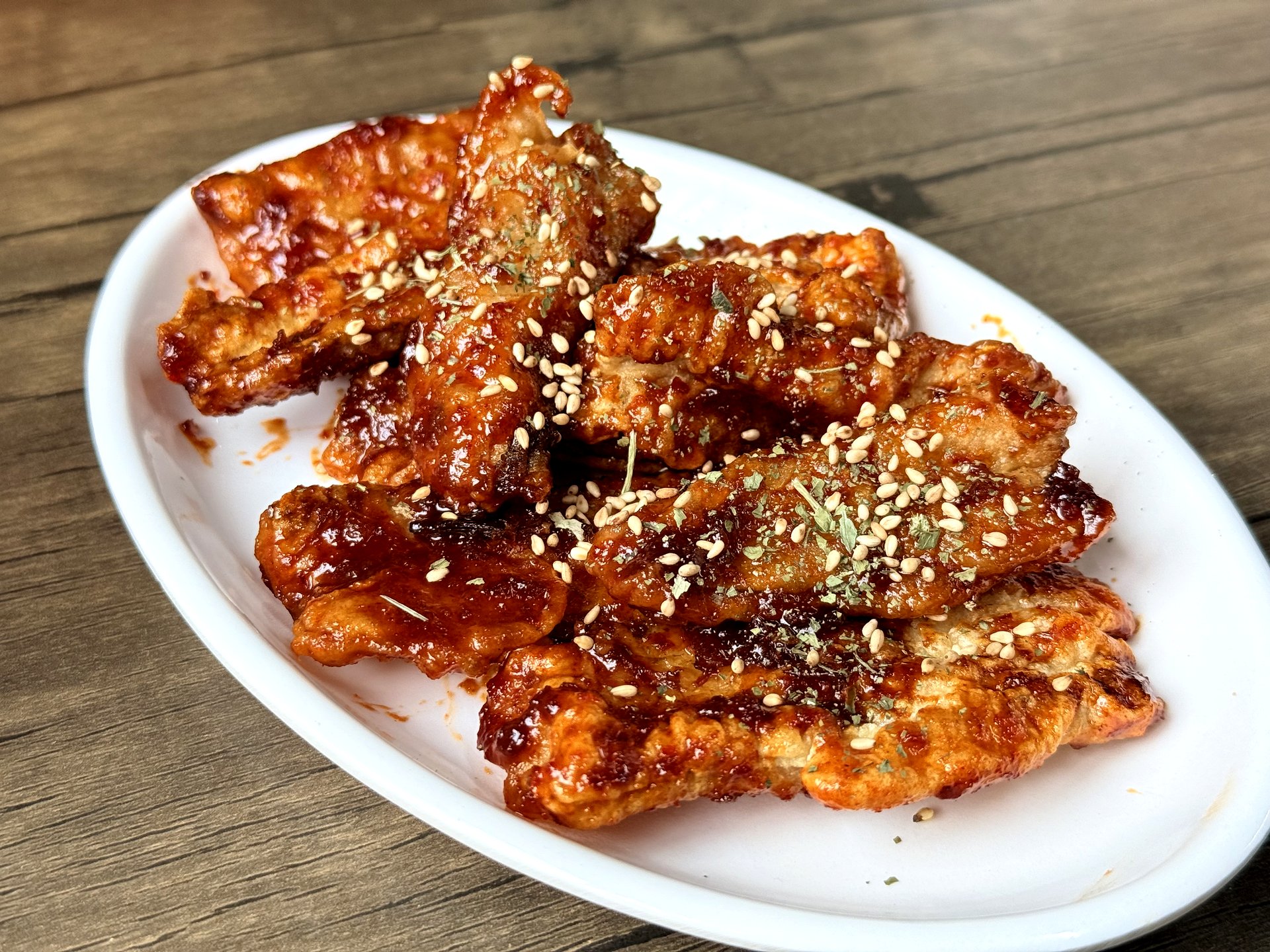 Samgeori Sikdang galchi-gangjeong - boneless cutlassfish pieces fried crisp and tossed in a glossy sweet-spicy red glaze with sesame seeds, on a white plate